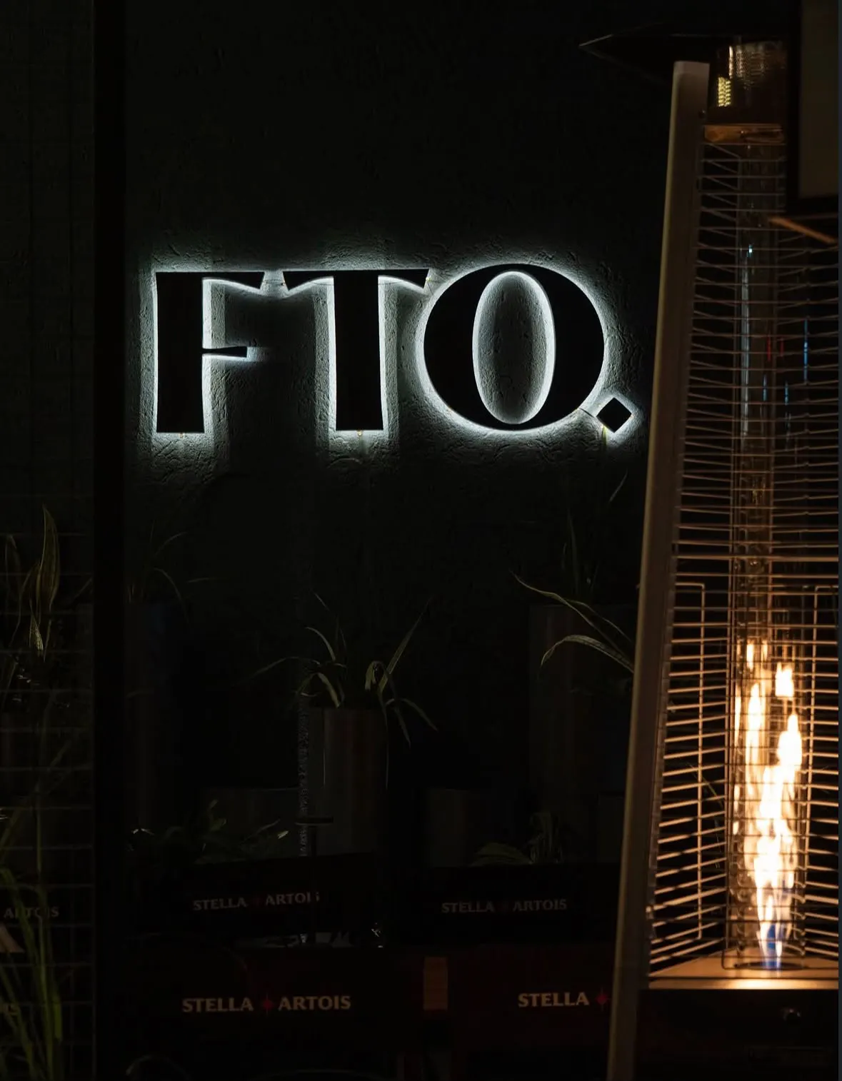 Cartel FTO. iluminado en la pared de Frato, de noche, junto a una estufa a gas encendida